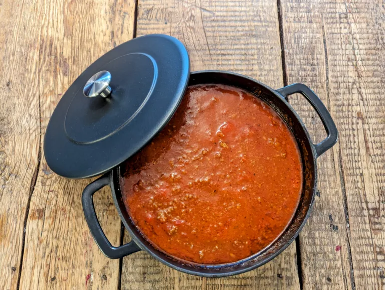 Recette rapide de sauce tomate à la viande dans une cocotte en fonte avec son couvercle sur une table en bois de grange.